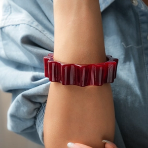 Dettaglio di un ampio bracciale in acrilico rosso traslucido con bordi ondulati