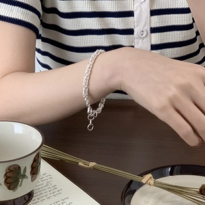 Detail of silver woven chain bracelet styled with a striped shirt and coffee