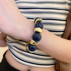 Detail of blue acrylic round beads and irregular golden metal charms on a worn bracelet