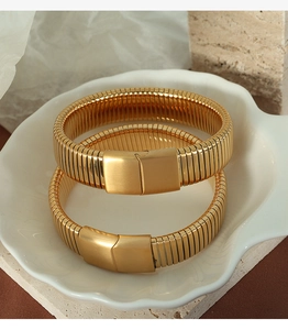 Detail view of gold stacked spring metal bracelets on white shell plate and silk backdrop