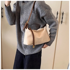 Detail of cream shoulder bag featuring brown contrast strap and leather tassel accent