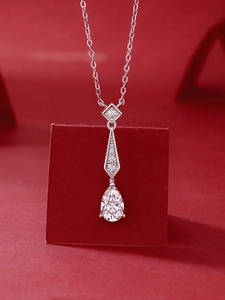 Detailed view of teardrop Moissanite pendant with silver chain on red velvet stand