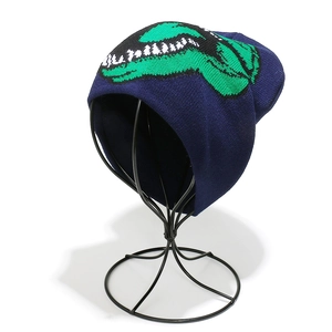 Detailed close-up of dark blue beanie showing green dinosaur knitted pattern on stand