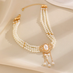 Detail of multi-layer white pearl necklace with gold pendant and tassel on beige silk