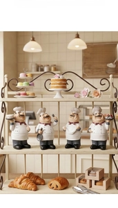 Close-up of four resin chef figurines holding cakes and pastries in a warm bakery setting