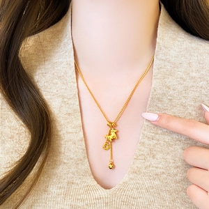 Detail of a gold zodiac horse pendant with tassel and coin on a beige sweater
