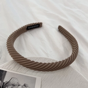 Detailed shot of brown ribbed fabric headband with handmade label on white textured background