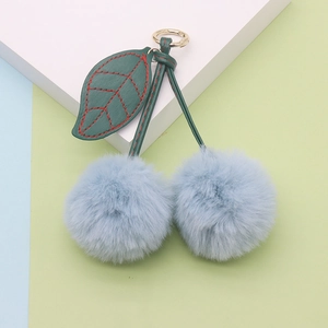 Close-up of light blue plush cherry keychain with green leather leaf and gold metal ring