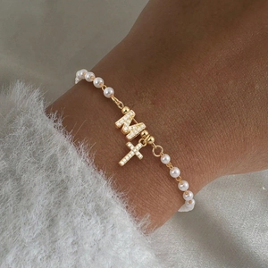 Bracelet de perles élégant avec lettre M dorée et charms croix sur un poignet