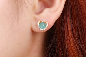 Macro shot of a heart-shaped gold earring with a green gemstone and white zircon accents