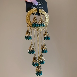 Close-up of golden Jhumka earrings with green beads and layered tassel bell details