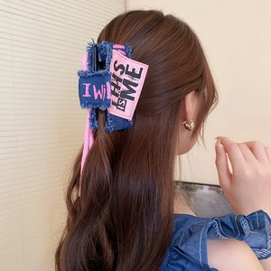 Detail of blue denim bow hair claw clip with pink 'THIS IS ME' text on hair