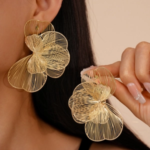 Macro shot of large golden hollow out flower earrings showing delicate metal line textures