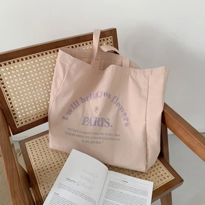Minimalist canvas tote bag in beige-pink with purple Paris embroidery on a woven chair