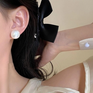 Close-up of elegant large round pearl earring and black satin bow hair clip on model