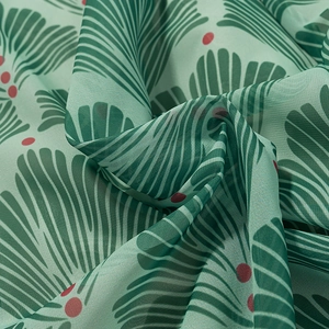 Detail of green chiffon fabric with leaf prints and red polka dots for slim long dress