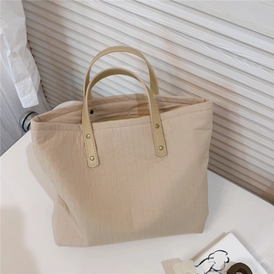 Detail of beige striped fabric tote bag featuring faux leather handles and metal rivets