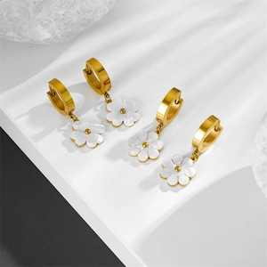 Gold earrings featuring white shell flower charms on a minimalist stone background