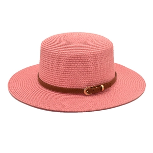 Detail of pink straw sun hat with wide brim and brown leather strap with gold buckle
