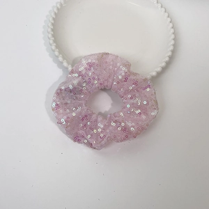 Detailed shot of a pink sequin mesh scrunchie hair tie on a white decorative plate