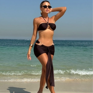 Three-piece black bikini set with gold metal rings and a wrap skirt on a beach