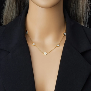 Detail of gold chain necklace with multiple white shell heart pendants worn on a model