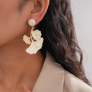 Detail of white raffia flower earrings with gold leaves on model for boho vacation style