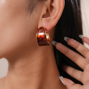 Detail view of tortoiseshell resin C-shaped hoop earrings with gold lining on a model