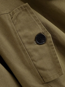 Close-up of olive green twill fabric and black button detail on military jacket