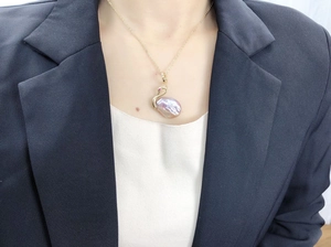 Détail du pendentif cygne en perle baroque mauve avec rubis sur une fine chaîne dorée