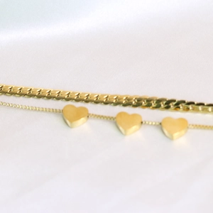 Close-up of dual-layer 18K gold stainless steel bracelet with heart charms on white silk