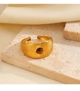 Detail of gold open ring with brown stone and radial texture on a stone surface