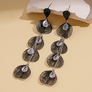 Détail de boucles d'oreilles pétales noirs ajourés avec pompons argentés et zircons
