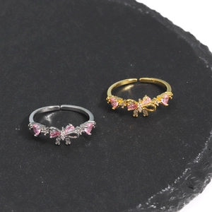 Elegant adjustable bow rings in gold and silver with pink heart stones on stone background