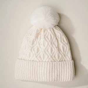 Close-up of white cable knit beanie with faux fur pom-pom and thick ribbed cuff detail