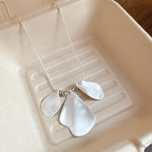 Detail of silver brushed petal pendants on a minimalist chain over a beige texture