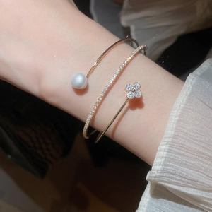 Detailed macro view of gold-tone clover and pearl open bangles on a female wrist