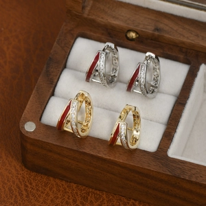 Detail of gold and silver hoop earrings with red enamel and zircon in a wood jewelry box