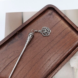 Close-up of vintage silver tassel hairpin with floral pendant on a wooden tray