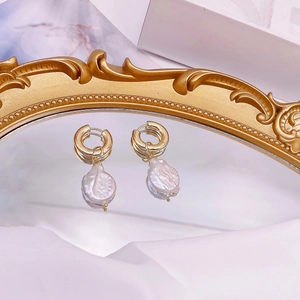 Baroque freshwater pearl hoop earrings with irregular gold charms on a mirror background