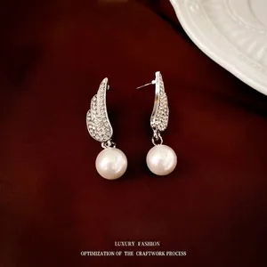 Detail of silver wing earrings with inlaid crystals and hanging white round pearl