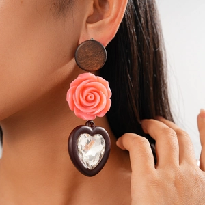 Détail de boucles d'oreilles bohèmes avec fleur en résine rose et cœur en cristal