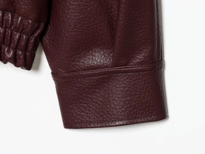 Détail d'une veste en similicuir bordeaux foncé avec texture grainée et coutures soignées
