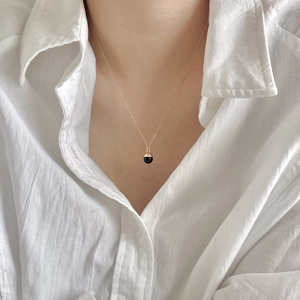 Minimalist gold chain necklace featuring a black onyx and gold ball pendant on a white shirt