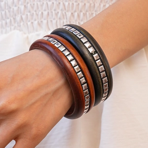Détail de bracelets en bois superposés rouge-brun et noirs avec rivets carrés argentés