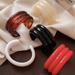 Close-up of five colorful thick resin bangles in amber, beige, black, white, and red
