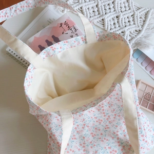 Flat lay of small floral cotton tote bag with notebooks and makeup for daily life style