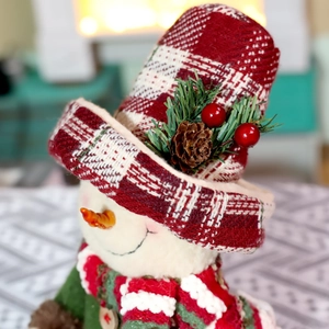 Detail-Nahaufnahme eines Weihnachts-Schneemanns mit rot-kariertem Hut und Zapfendekoration