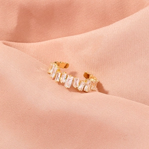Detail of gold ear cuff with rectangular crystals on a peach fabric background