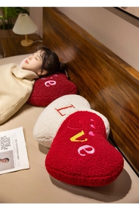 Detail of red and cream heart-shaped plush pillows with LOVE embroidery on sheep wool fabric